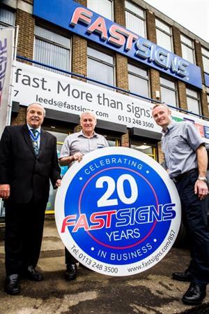 3 men holding Fastsigns 20 Years signage