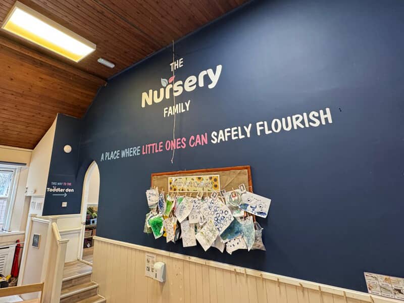 An image of a dark wall with graphics that say, "The Nursery Family" and "A place where little ones can safely flourish."